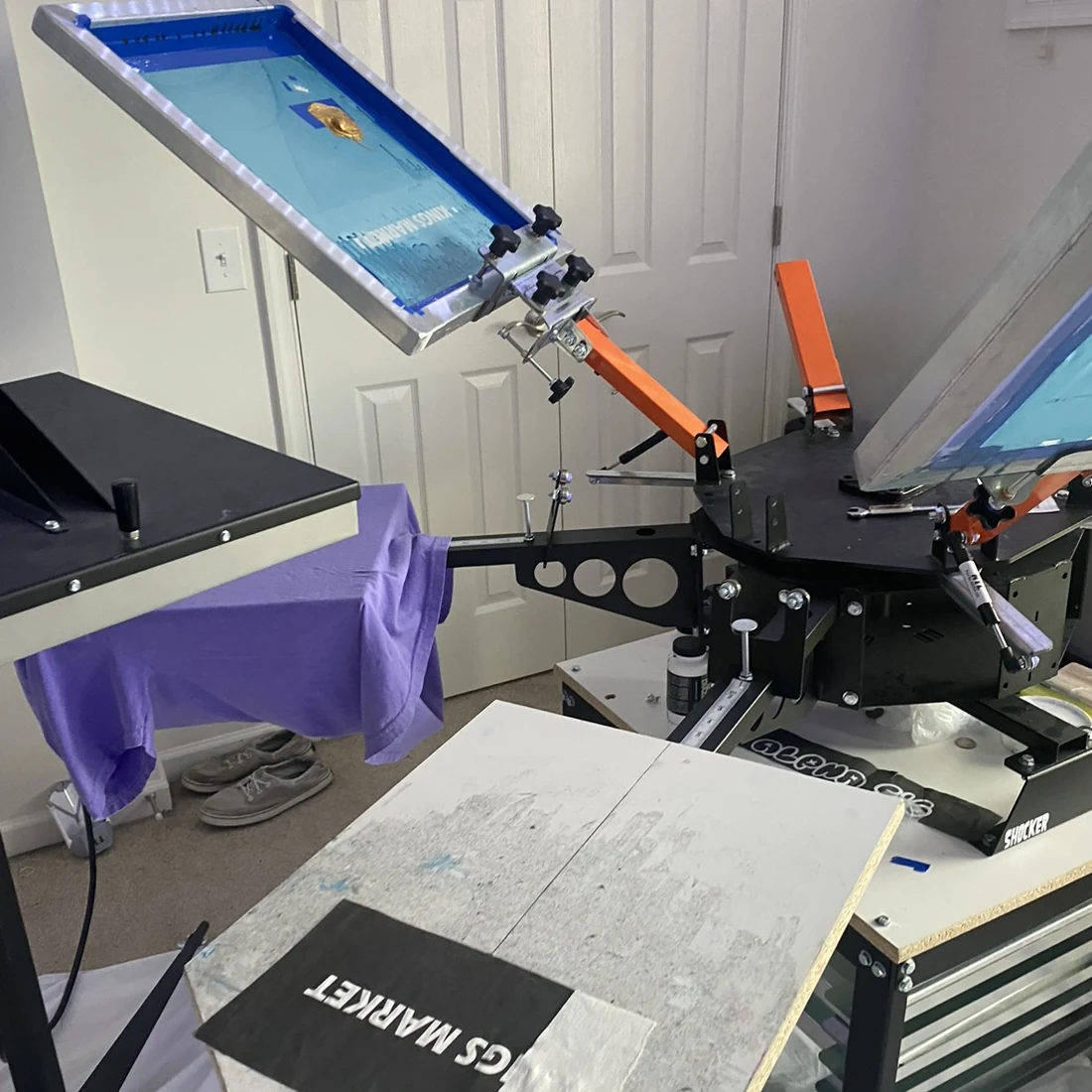 A screen printing press with a screen loaded and a shirt on the platen