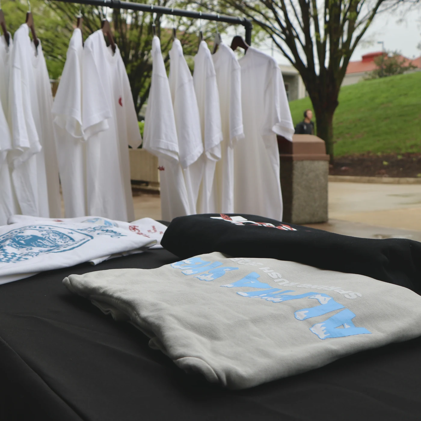 A campus apparel pop-up with shirts on a rack and folded crewnecks on the table