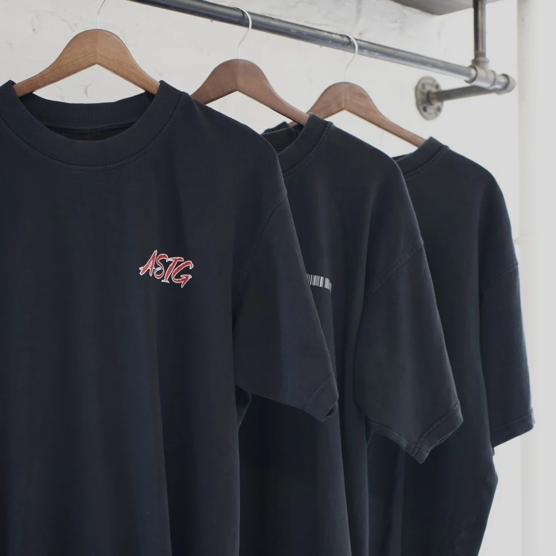 Black shirts with red ASIG embroidery hanging on wooden hangers
